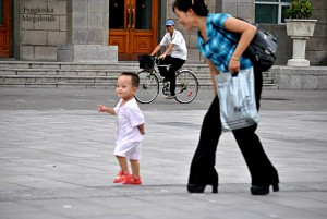 Νεαρή μητέρα παίζει με το μωρό της στην πλατεία Κιμ Ιλ Σουνγκ υπο το βλέμμα του ποδηλάτη που παρακολουθεί χαμογελώντας
