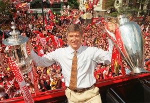 ARSENAL FC MANAGER HOLDS THE FA CUP AND PREMIER LEAGUE TROPHIES.